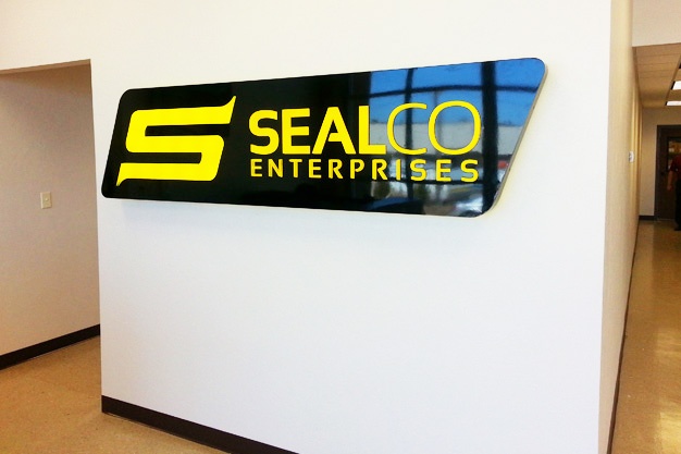 Picture of a logo wall sign on an inside wall, with illuminated yellow letters on a black background, and shiny.